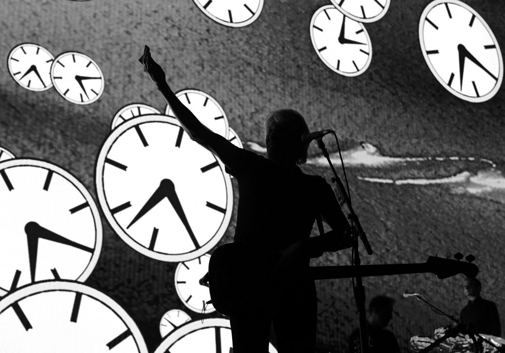 sillhouette of roger waters with a background of clocks behind him