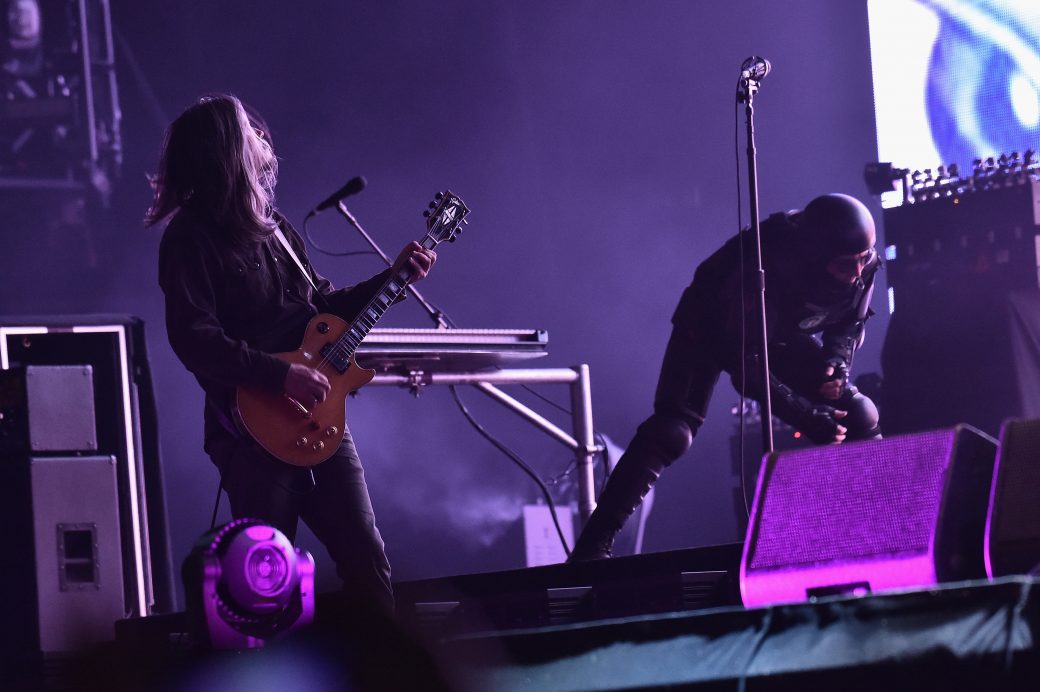 the guitar player and singer of TOOL perform wearing a space suit perform onstage with a purple background.