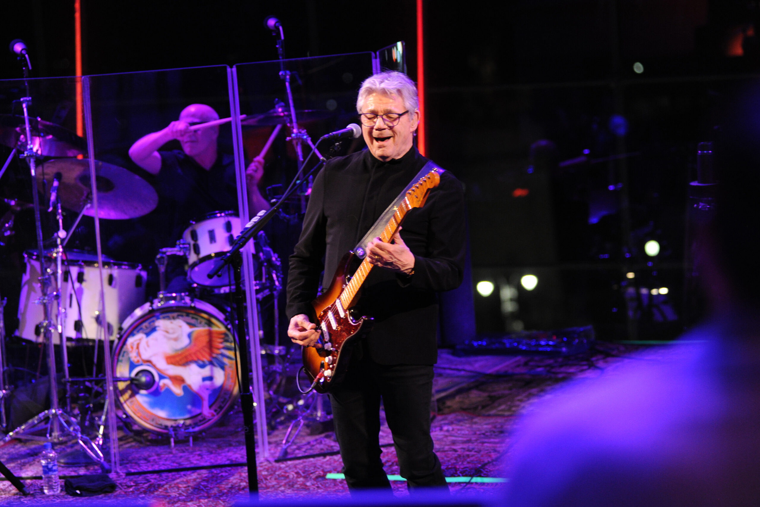 Steve Miller stands in front of the mic playing guitar
