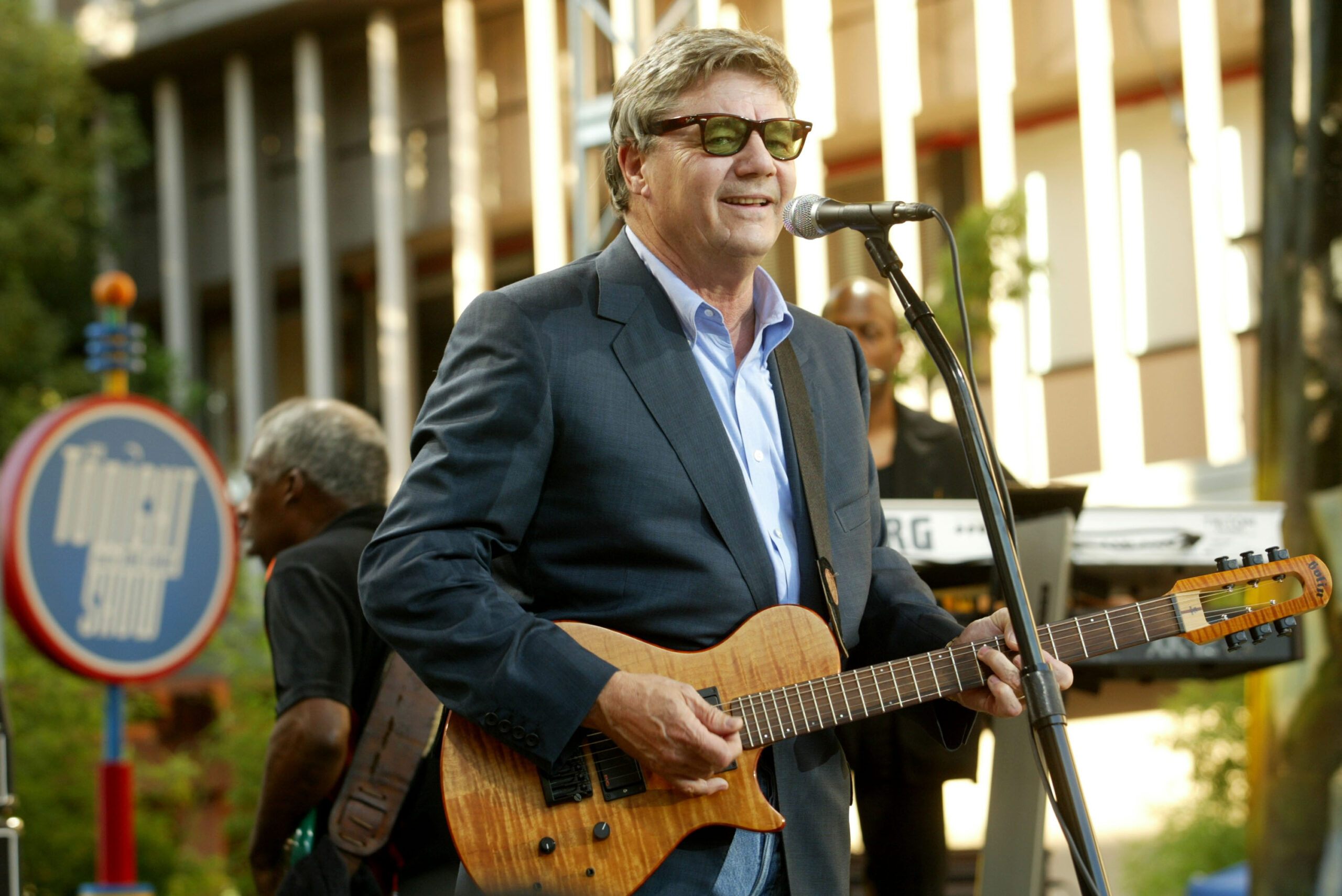 steve miller wearing sunglasses playing guitar in front of a mic