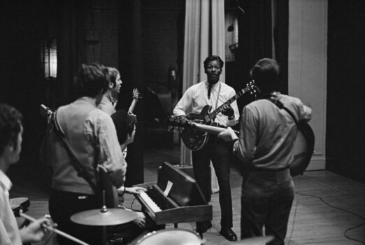 Band members look onto leader Chuck Berry, holding a guitar, backstage