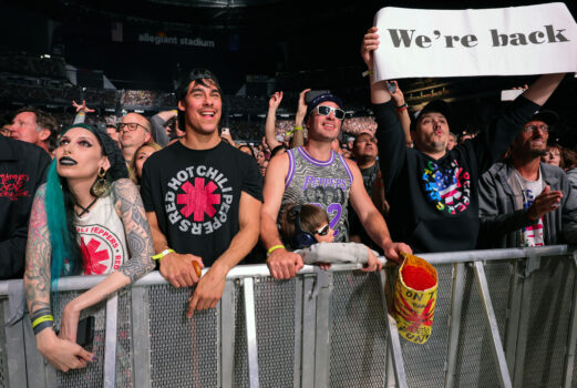 a row of fans behind a fence wearing red hot chili pepper t shirts and gear