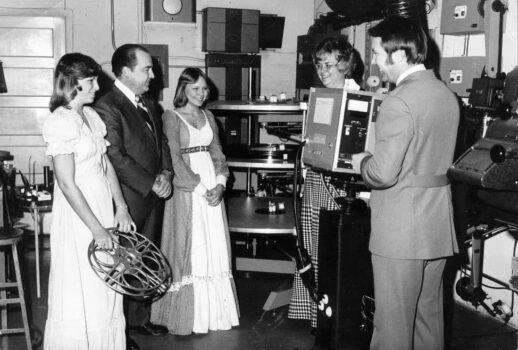 archival photo of 4 people looking at a movie projector